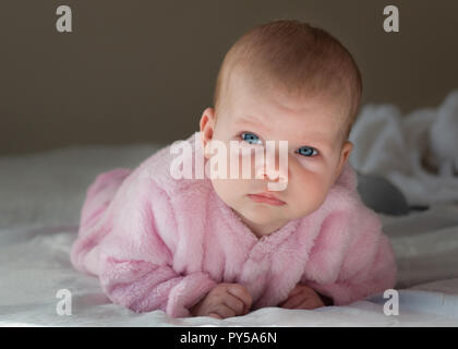 Baby Girl portant sur son ventre à la recherche jusqu'à l'appareil photo avec des yeux bleu rose porte close up de son visage. Banque D'Images