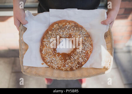 Baker tenant un pain tressé Garnie de noix et graines dans un panier en osier à l'extérieur d'une boulangerie. Banque D'Images