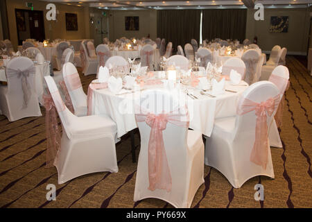 Salle de réception de mariage dans un hôtel avec des tables rondes guest avec nappe blanche et un ruban rose sur des chaises Banque D'Images