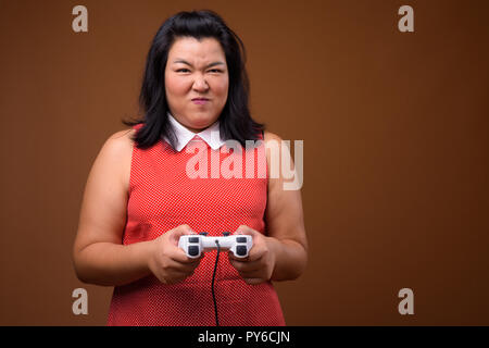 Belle femme asiatique de l'embonpoint à jouer à des jeux vidéo en utilisant un contrôleur de jeu Banque D'Images