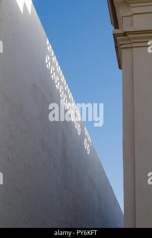 Coin d'une chambre et d'une clôture blanche avec un motif de soleil à travers une clôture sur le toit. Ciel bleu. Faro, Portugal. Banque D'Images