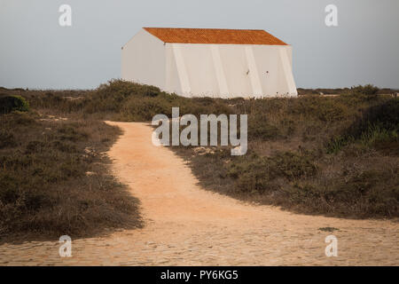 Forteresse construite sur les falaises. Les buissons à sec à l'automne. Bâtiment blanc avec un toit orange. Ciel nuageux ciel pluvieux. Sentier de sable. Sagres, Portugal. Banque D'Images