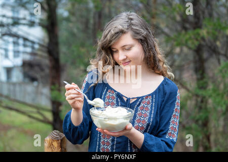 Jeune femme à l'extérieur, en plein air, holding glass bowl full of des végétalien premières bananes vanille, crème glacée, l'écopage écope avec une cuillère d'une main Banque D'Images