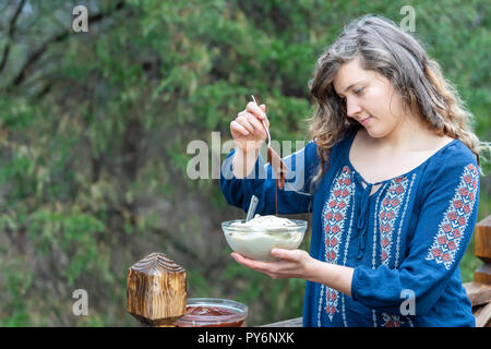 Jeune femme à l'extérieur, à l'extérieur, tenant bol en verre composé de végétalien premières, glace vanille, sauce au chocolat ajouter la cuillère de liquide Banque D'Images