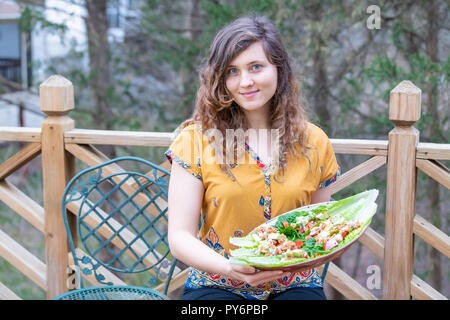 Jeune femme assise à l'extérieur, en plein air, holding salad de feuilles de laitue, tomates, concombres, avocat, l'écrou de la viande végétalien premières fait maison Banque D'Images