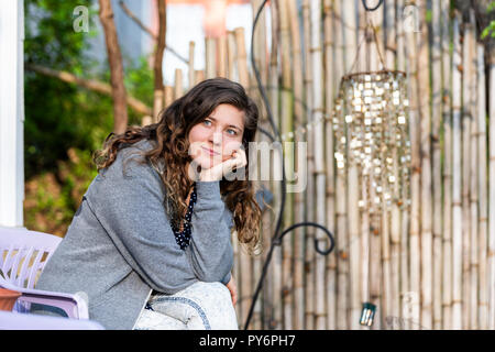 Gros plan du visage jeune femme à happy smiling en bambou zen garden avec décorations brillant Wind Chimes sitting on chair Banque D'Images