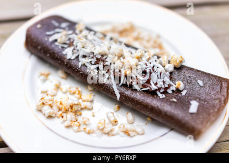 Gros plan macro de dessert crêpes au chocolat, enveloppement chips de riz, flocons de noix de coco, fait en bouteille avec des bananes sur la plaque Banque D'Images