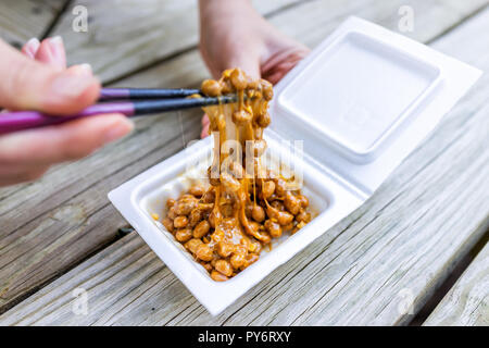 Gros plan du hand holding chopsticks, mélange de soja fermentée Natto japonais asiatique lave visqueuse, collante, repas à texture récipient en polystyrène fort Banque D'Images