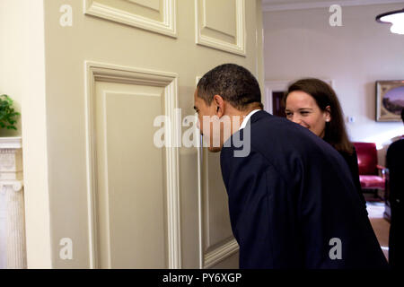 Le président Barack Obama regarde à travers le judas de la porte du bureau ovale comme son secrétaire personnel Katie Johnson montres 3/12/09. Photo Officiel de la Maison Blanche par Pete Souza Banque D'Images