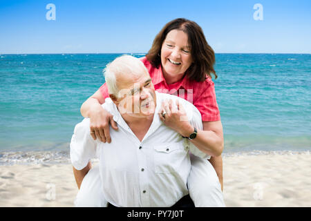 Portrait Of A Happy Senior Man Giving Piggyback à sa femme At Beach Banque D'Images