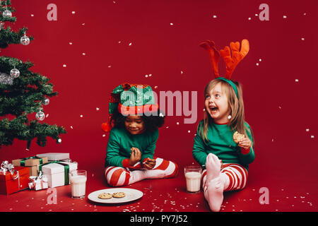 Les petites filles appréciant les flocons de neige tomber assis à côté d'un arbre de Noël. Dans Fantaisie enfants Vêtements de Noël Noël t'asseoir à côté d'une Banque D'Images