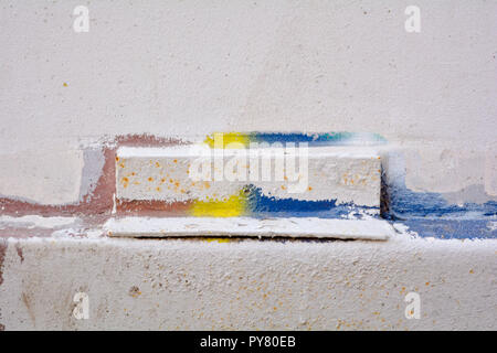 Le vieux mur est peint avec peinture blanche et le fragment sélectionné est peint en bleu, rouge et jaune Banque D'Images