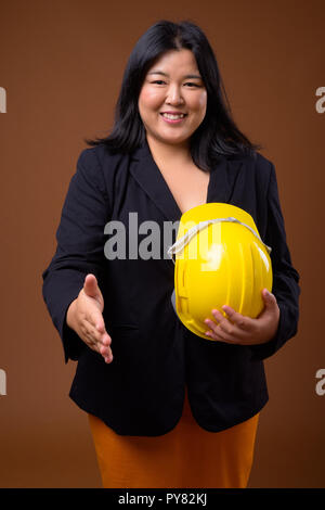 Happy Asian businesswoman holding casque de protection et poignée offrant Banque D'Images