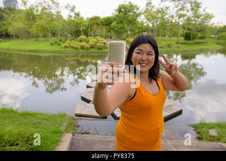 Belle femme asiatique en prenant de l'embonpoint avec selfies téléphone mobile en park Banque D'Images