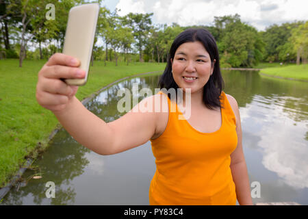 Belle femme asiatique de l'embonpoint en tenant l'extérieur selfies Banque D'Images