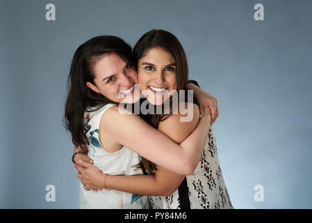 Deux jeunes smiling girl friends hugging sur fond de studio Banque D'Images