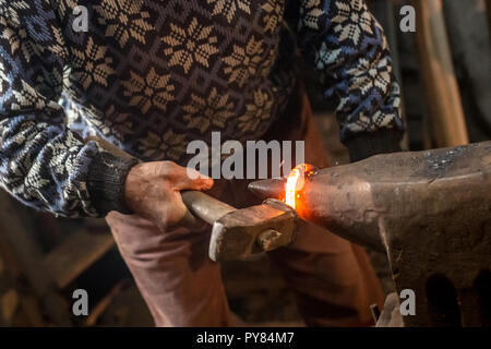 Ancien forgeron forge manuellement le métal en fusion à l'aide d'un marteau sur l'enclume. Banque D'Images