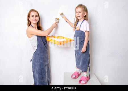 Réparation dans l'appartement. Famille heureuse mère et fille en bleu peintures tabliers le mur avec peinture blanche Banque D'Images