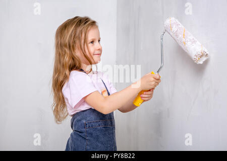 Réparation dans l'appartement. Famille heureuse mère et fille en bleu peintures tabliers le mur avec peinture blanche. Petite fille peint le mur avec rouleau Banque D'Images