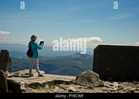 Une femme aux cheveux gris prend une photo de la vue avec un iPad au sommet du Mont Snowdon, le parc national de Snowdonia, Gwynedd, au nord du Pays de Galles, Royaume-Uni Banque D'Images