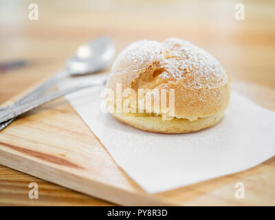 Éclairs délicieux saupoudrée de sucre glace et de cuillères sur planche à découper en bois sur la table. Banque D'Images