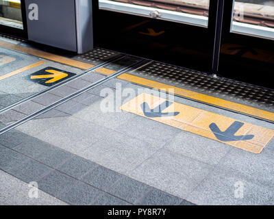 Zone d'attente sur une station du Skytrain. Flèche jaune panneau indiquant la ligne de sécurité et à l'entrée et à la sortie de la porte sur le sol. Banque D'Images