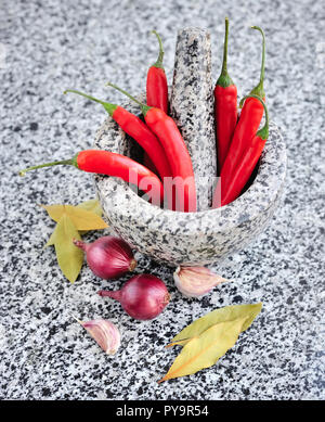 Mortier et pilon en pierre avec des légumes sur une table de granit Banque D'Images