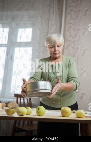 Une femme âgée faire peu de tartes. La farine de tamisage Banque D'Images