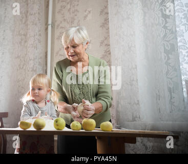 Une femme âgée ce qui fait d'apple peu des tartes à la maison. Sasser la farine avec petite fille. Banque D'Images