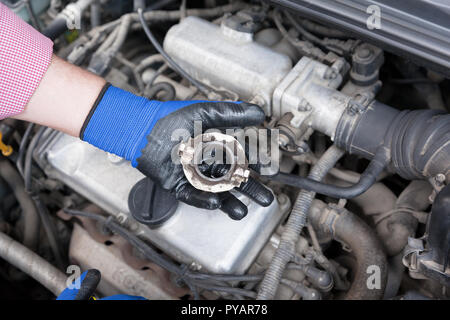 Mécanicien Auto portant des gants de travail holding old la butée d'embrayage sur le moteur d'un véhicule Banque D'Images