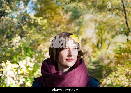 Portrait de jeune femme en congé d'automne avec l'écharpe sur sa tête. Feuille d'érable sur les cheveux d'une personne de sexe féminin dans l'article beau vert et jaune natur Banque D'Images