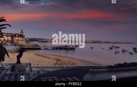 Vide de sable Praia do Ribeiro et bateaux de pêche une baie avec coucher du soleil magenta à Cascais, Portugal Banque D'Images