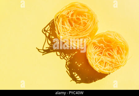 Les pâtes italiennes à sec appelé cheveux d'ange sur un fond jaune , deux nids de pâtes jaunes ,drôle , composition studio shot , vue d'en haut Banque D'Images
