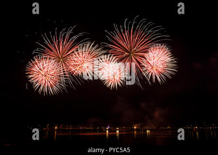 Explosions de fusées d'artifice rouge géant dans la sombre nuit au lac Banque D'Images