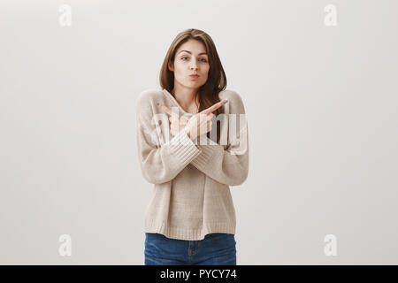 Demander à quelqu'un d'autre je suis dehors. Portrait de haussant clueless mignon femelle traversant les mains sur la poitrine et dirigées dans les deux sens avec l'index, le sourire et le fait de ne pas connaître sur fond gris Banque D'Images