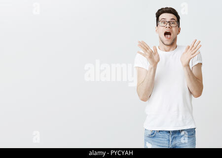 Studio shot of impressionné et surprirsed jeune homme blanc dans les verres debout côté droit de copie espace laissant tomber la mâchoire de mains dans l'étonnement et de réagir aux chocs super prix bas Banque D'Images