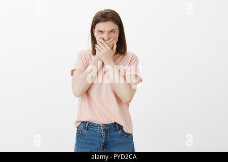 Elle n'est pas te dire mot. Portrait de femme en colère offensé reste sans voix, couvrant la bouche avec les deux paumes, fronçant et à la recherche de dessous le front avec la haine et la colère, debout au-dessus de mur gris Banque D'Images