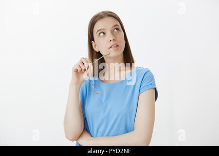 Girl dreaming, pensant Combien dépensent les loisirs. Portrait de smart bon-à la femme européenne, mordre, lunettes de rim à la recherche au coin supérieur droit, être intrigué et intéressé par quelque chose Banque D'Images