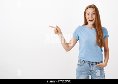 La chance de visiter le magnifique endroit. Portrait de charmant heureux et heureux divertir bon-à la jeune fille rousse avec des taches de rousseur haletant avec happy sourire impressionné d'être amusé pointant vers la gauche Banque D'Images