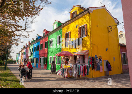 Burano, Italie - Octobre 2018 : les habitants parler devant une boutique vendant de la dentelle, avec une vue sur les maisons colorées à côté. Banque D'Images