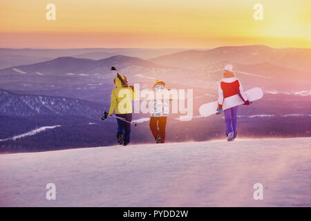 Trois amis skieurs et snowboarders sont la marche en montagne au coucher du soleil Banque D'Images