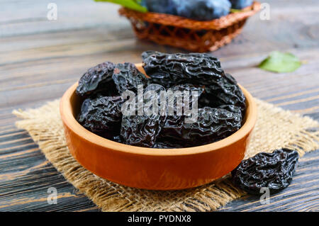 Les pruneaux dans un bol d'argile et de prunes fraîches, feuilles sur une table en bois. Pruneaux frais pour la vie en bonne santé. Banque D'Images