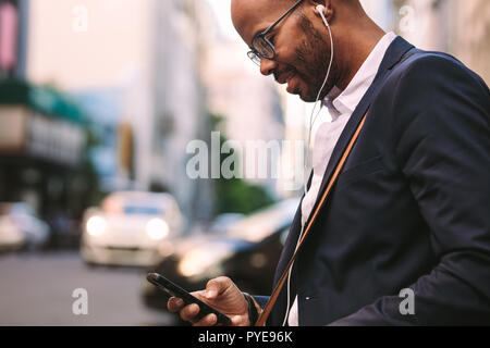 Heureux homme millénaire la navette avec un smartphone. Hommes et femmes d'écouter de la musique grâce à ses écouteurs alors que la marche à l'extérieur sur Ville Banque D'Images