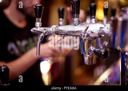 Appuyez sur la bière avec des gouttes sur un arrière-plan flou bartender pouring beer dans un verre. Banque D'Images