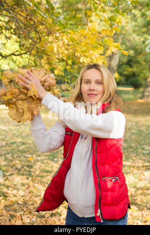 Cheerful young woman throwing leaves in autumn forest Banque D'Images