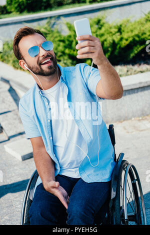 Bel homme en fauteuil roulant sticking tongue out et en tenant avec selfies sur smartphone street Banque D'Images