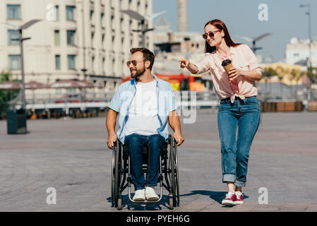 Jolie petite amie pointant sur quelque chose de beau mec en fauteuil roulant sur la rue Banque D'Images