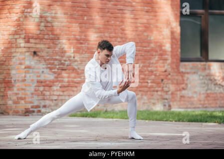 Beau jeune danseur dans des vêtements blancs pratiquant sur street Banque D'Images