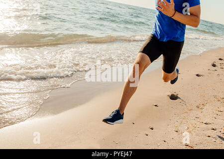 Jambes courir le long du canal de l'athlète en laissant des traces de pas dans le sable de plage Banque D'Images