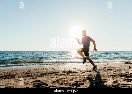 Runner homme courir le long de plage de sable fin dans le coucher du soleil Banque D'Images